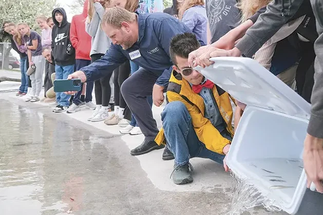 Patrick Croft, CEO of CROFT, holding his camera phone horizontally to capture students emptying live fish from a cooler