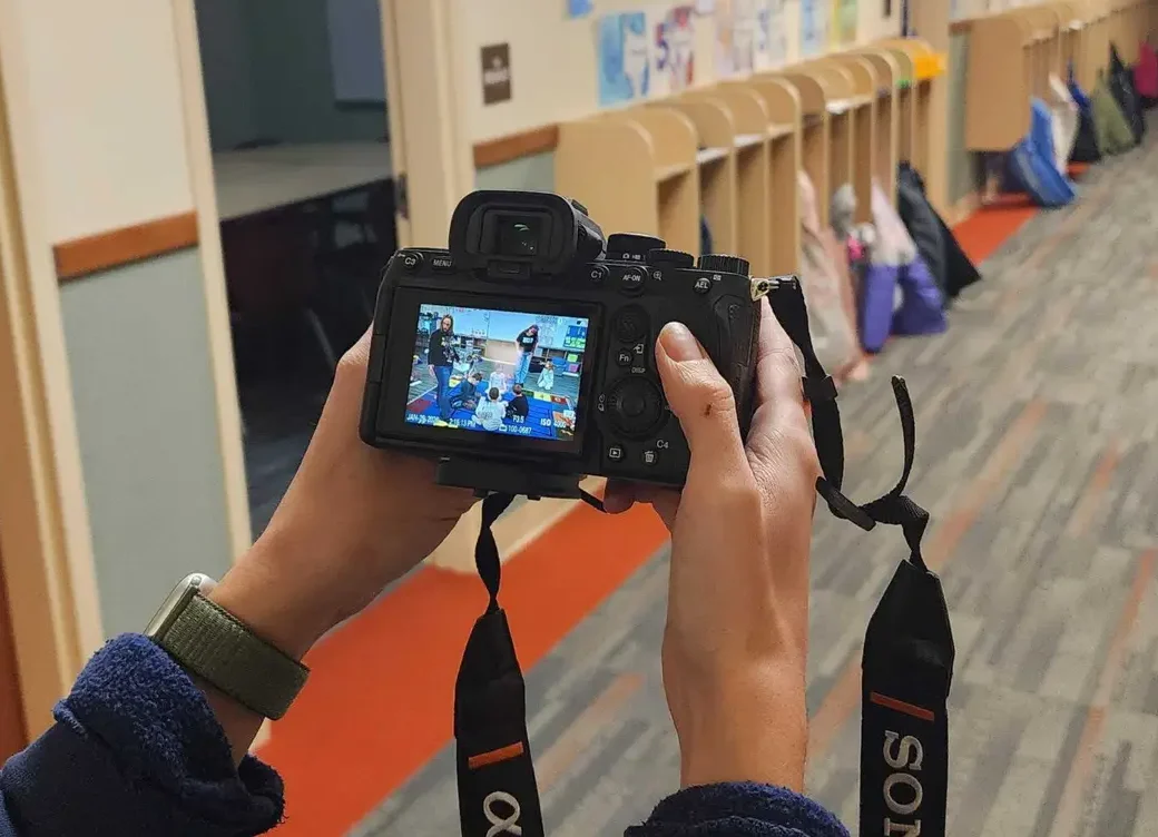 Photographer holding camera capturing classroom activity in school hallway